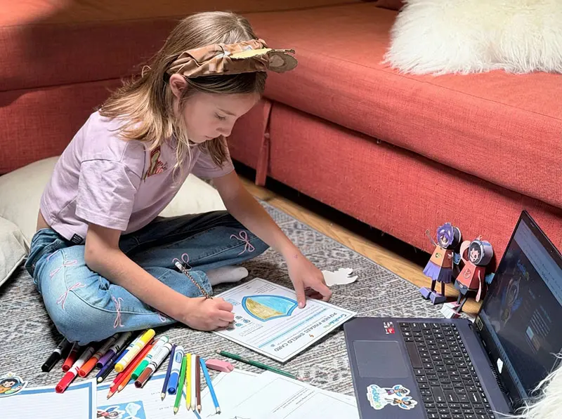 A girl working on a CreatableMe activity on the floor at home